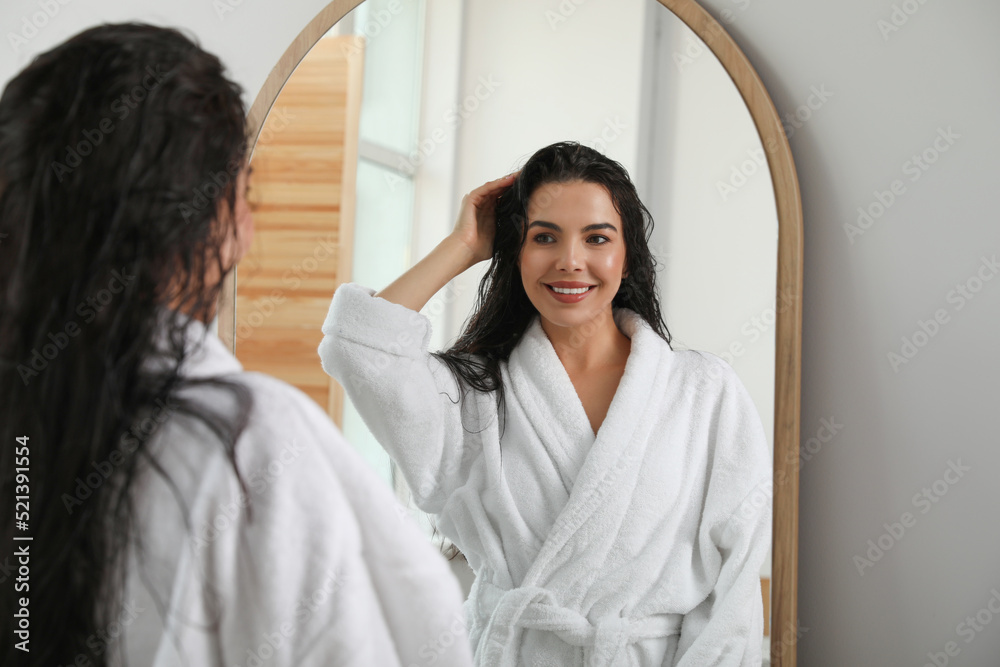 Beautiful young woman in bathrobe standing near mirror indoors Beautiful young woman in bathrobe standing near mirror indoors