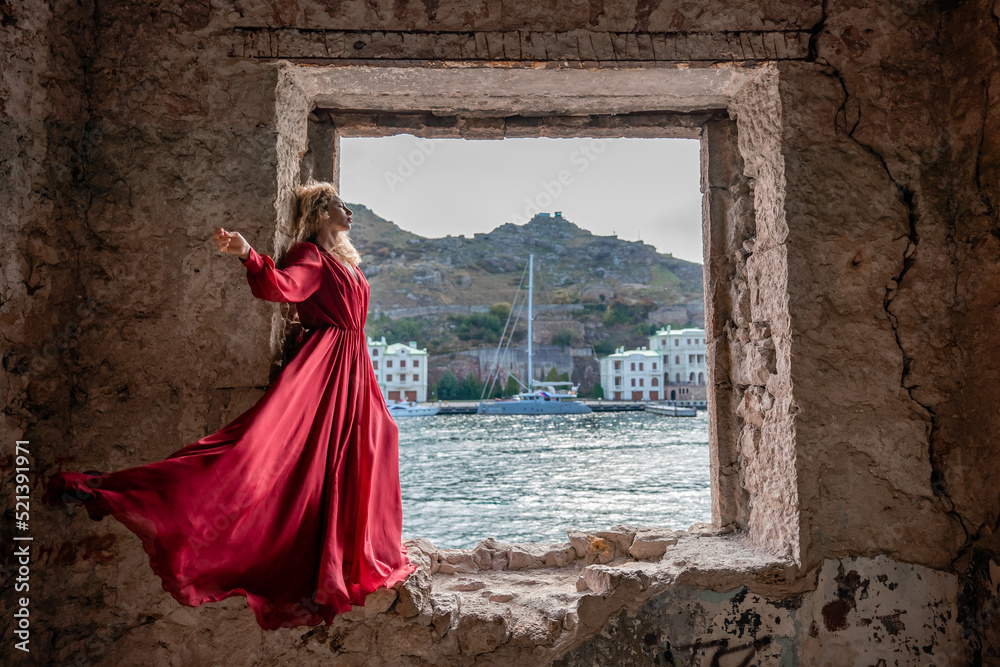 View of Balaklava Bay through an arched balcony in oriental style. The girl in a long red dress stands with her back. Abandoned mansion on the Black Sea coast View of Balaklava Bay through an arched balcony in oriental style. The girl in a long red dress stands with her back. Abandoned mansion on the Black Sea coast