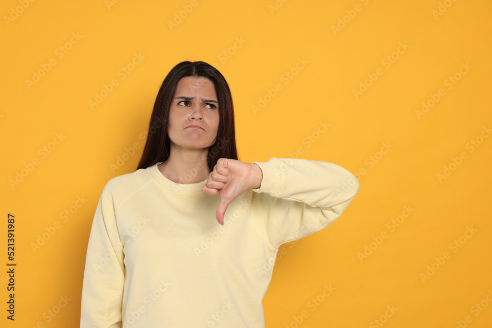 Young woman showing thumb down on orange background Young woman showing thumb down on orange background