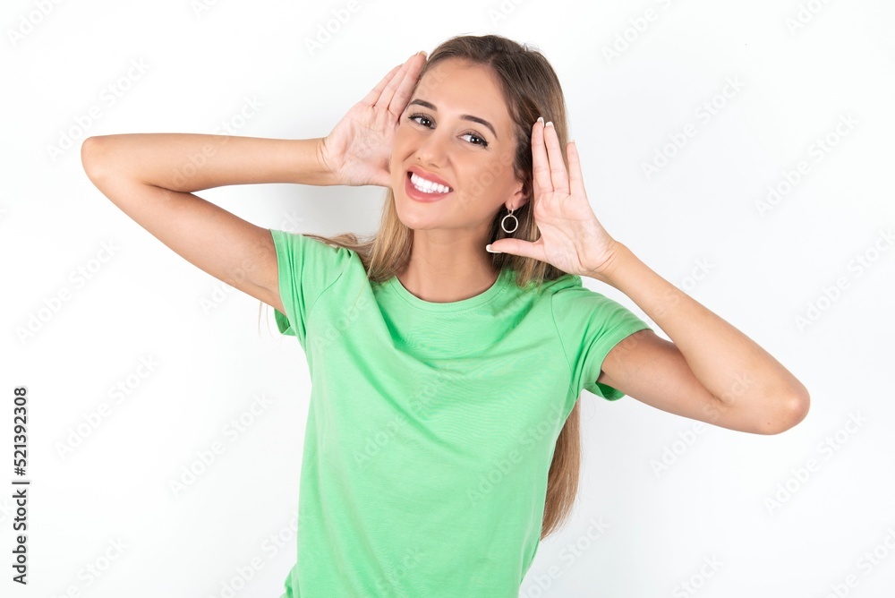 young beautiful woman wearing green T-shirt over white background, Trying to hear both hands on ear gesture, curious for gossip. Hearing problem, deaf young beautiful woman wearing green T-shirt over white background, Trying to hear both hands on ear gesture, curious for gossip. Hearing problem, deaf