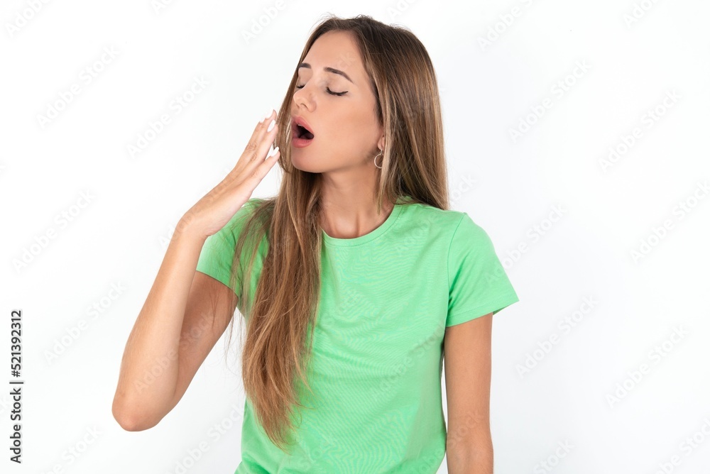 young beautiful woman wearing green T-shirt over white background, being tired and yawning after spending all day at work. young beautiful woman wearing green T-shirt over white background, being tired and yawning after spending all day at work.