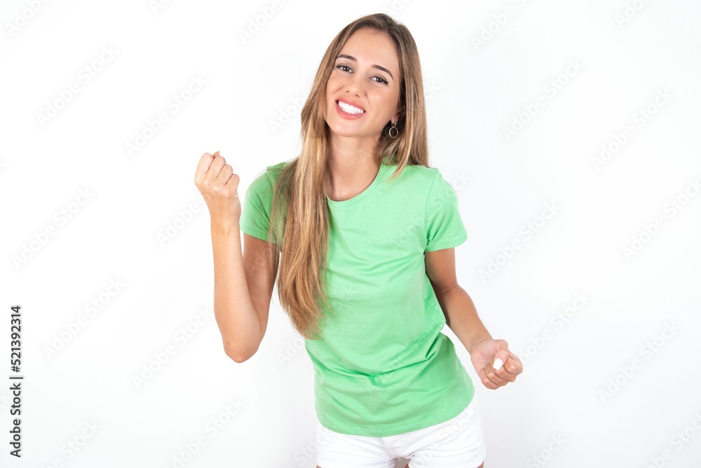 young beautiful woman wearing green T-shirt over white background, celebrating surprised and amazed for success with arms raised and eyes closed. Winner concept. young beautiful woman wearing green T-shirt over white background, celebrating surprised and amazed for success with arms raised and eyes closed. Winner concept.