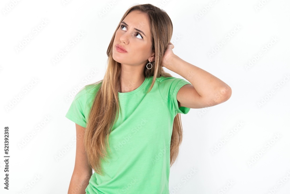 young beautiful woman wearing green T-shirt over white background, confuse and wonder about question. Uncertain with doubt, thinking with hand on head. Pensive concept. young beautiful woman wearing green T-shirt over white background, confuse and wonder about question. Uncertain with doubt, thinking with hand on head. Pensive concept.