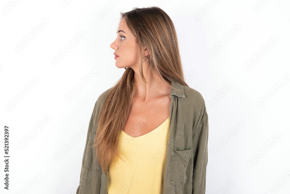 Close up side profile photo young beautiful woman wearing green overshirt over white background, not smiling attentive listen concentrated Close up side profile photo young beautiful woman wearing green overshirt over white background, not smiling attentive listen concentrated