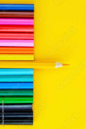 Set of colored pencils on a bright yellow background. One pencil in the center is pushed forwardr. Drawing materials, leadership concept, being different. Top view photo