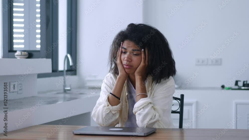 Young worried woman sitting at wooden table with a laptop, in a home interior, looking aside with despair and feeling depressed and unmotivated. Depression, collapse, failure, sadness. Young worried woman sitting at wooden table with a laptop, in a home interior, looking aside with despair and feeling depressed and unmotivated. Depression, collapse, failure, sadness.