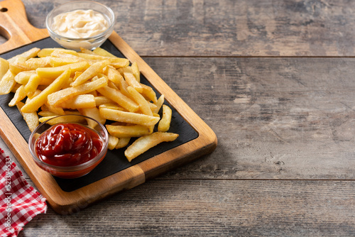 Fried potatoes with ketchup and mayonnaise on wooden table. Copy space