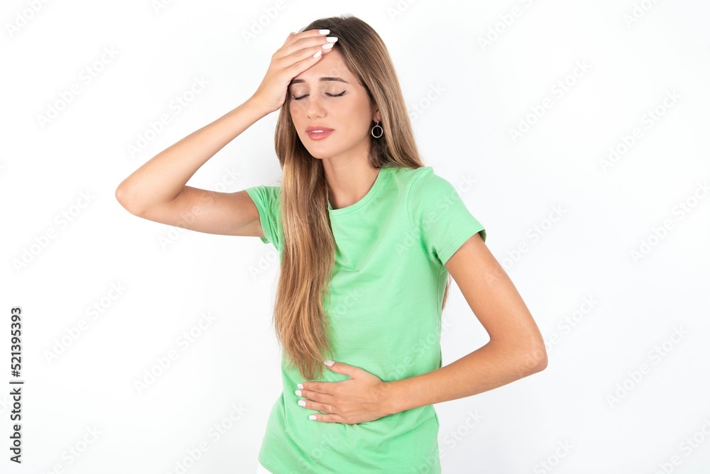 young beautiful woman wearing green T-shirt over white background, Touching forehead for illness and fever, flu and cold, virus sick. young beautiful woman wearing green T-shirt over white background, Touching forehead for illness and fever, flu and cold, virus sick.