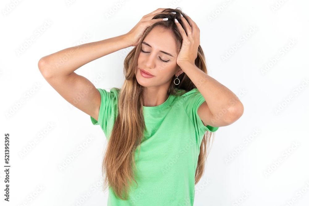 young beautiful woman wearing green T-shirt over white background, suffering from strong headache desperate and stressed because of overwork. Depression and pain concept. young beautiful woman wearing green T-shirt over white background, suffering from strong headache desperate and stressed because of overwork. Depression and pain concept.