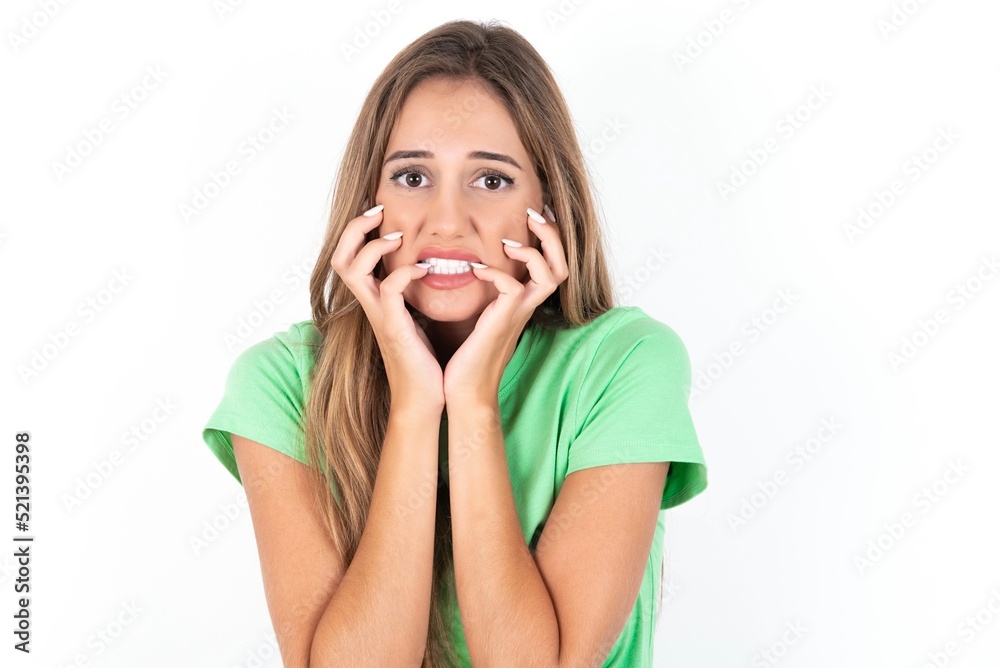 Fearful young beautiful woman wearing green T-shirt over white background, keeps hands near mouth, feels frightened and scared, has a phobia, Shock and frighted concept. Fearful young beautiful woman wearing green T-shirt over white background, keeps hands near mouth, feels frightened and scared, has a phobia, Shock and frighted concept.