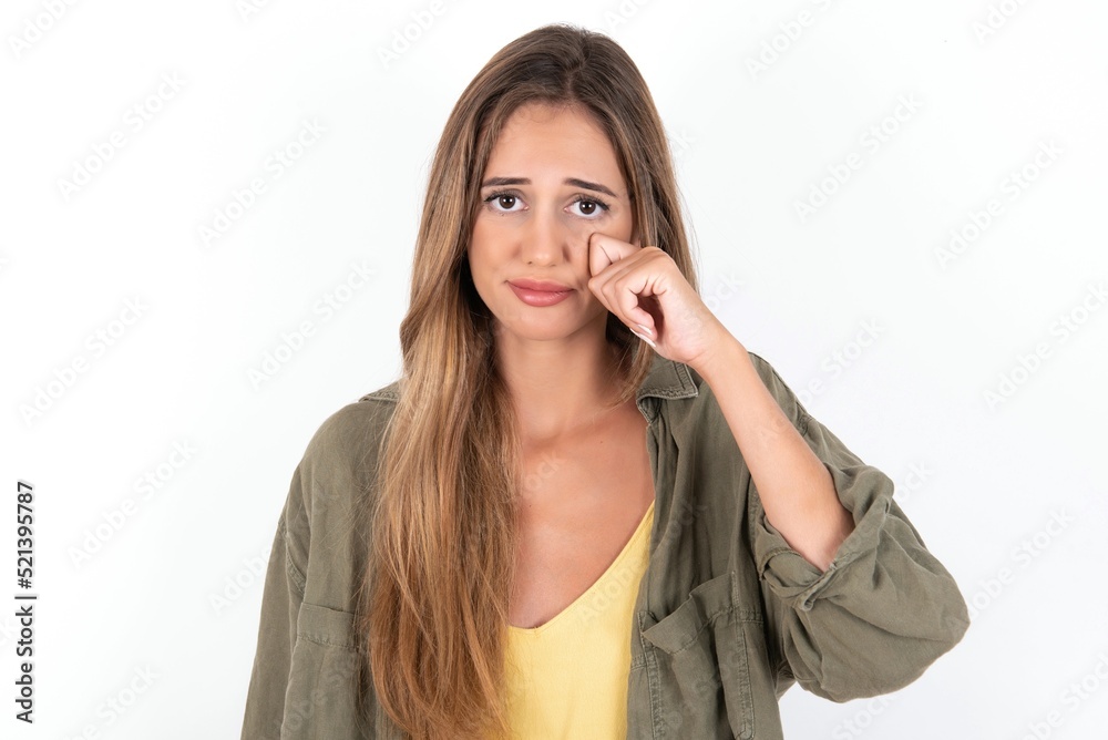 Disappointed dejected young beautiful woman wearing green overshirt over white background wipes tears stands stressed with gloomy expression. Negative emotion Disappointed dejected young beautiful woman wearing green overshirt over white background wipes tears stands stressed with gloomy expression. Negative emotion