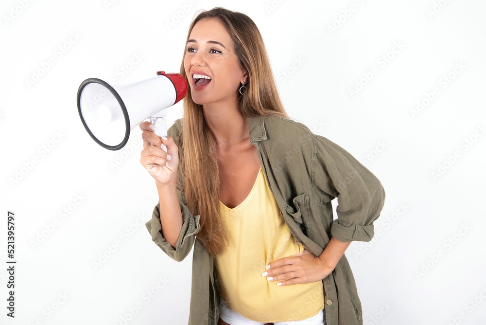 Funny young beautiful woman wearing green overshirt over white background People sincere emotions lifestyle concept. Mock up copy space. Screaming in megaphone. Funny young beautiful woman wearing green overshirt over white background People sincere emotions lifestyle concept. Mock up copy space. Screaming in megaphone.