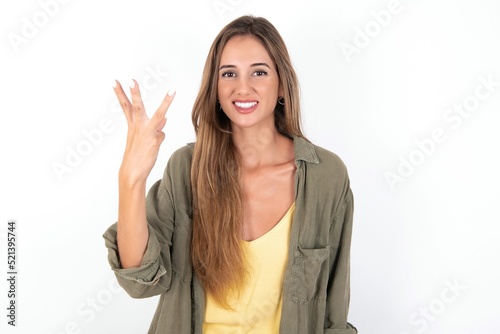 young beautiful woman wearing green overshirt over white background smiling and looking friendly, showing number three or third with hand forward, counting down
