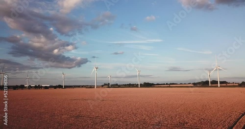 medium angle drone shot moving forwards towards wind turbines over a field during a stunning golden hour sunset in Bedfordshire, uk on a sunny summers day photo
