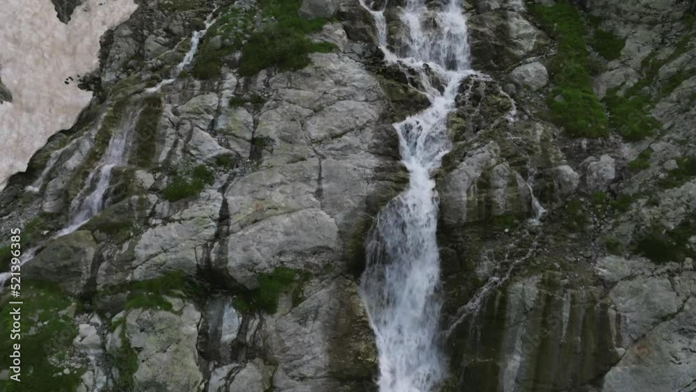 Aerial view of a glacial waterfall high in the mountains on a sunny day. Close up of a tall waterfall Aerial view of a glacial waterfall high in the mountains on a sunny day. Close up of a tall waterfall