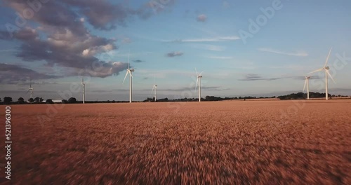Fast moving low angle drone shot moving forwards towards wind turbines over a field during a beautiful golden hour sunset in Bedfordshire, uk on a sunny summers day photo