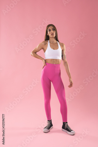 Fototapeta Naklejka Na Ścianę i Meble -  A young female trainer in pink and white sportswear poses standing isolated on a pastel light pink background. Training sport concept.