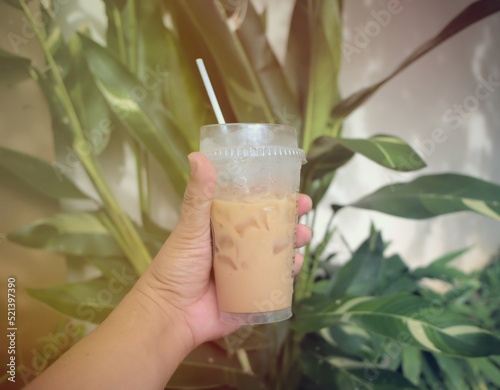Coffee cup in hand. Clear plastic glass. Iced coffee. Tree background. Sunlight. Drink.
