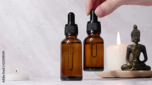 A woman puts a jar of essential oil. Spa treatment bottle of natural organic oil essence serum collagen. Aromatic candle and Buddha on white background. Beautiful woman hands.