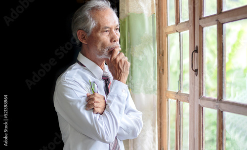 Contemplative elderly Asian businessman looking through the window