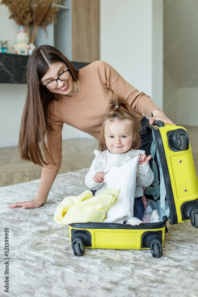 Traveling with children. Happy young mother with little toddler kid packs clothes in suitcase Traveling with children. Happy young mother with little toddler kid packs clothes in suitcase