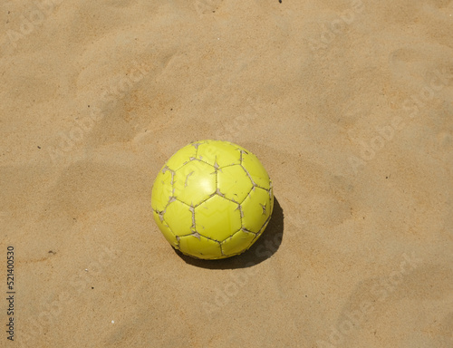 A picture of yellow ball on the sandy beach used for beach soccer.