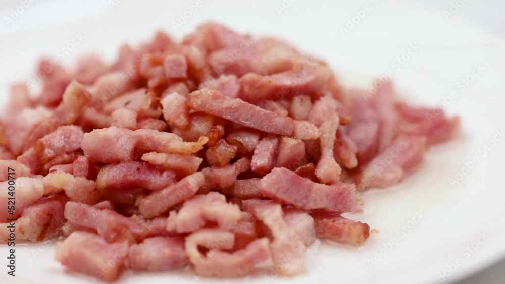 Sliced and fried bacon served on the white plate. Closeup macro shot of the food. Sliced and fried bacon served on the white plate. Closeup macro shot of the food.