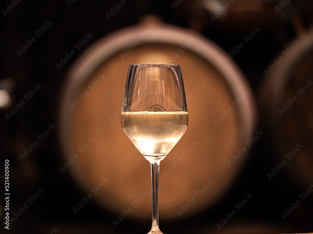 White wine in a glass with wooden barrel in the background - obrazy, fototapety, plakaty 