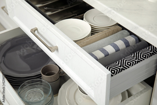 Open drawers of kitchen cabinet with different dishware and towels, closeup