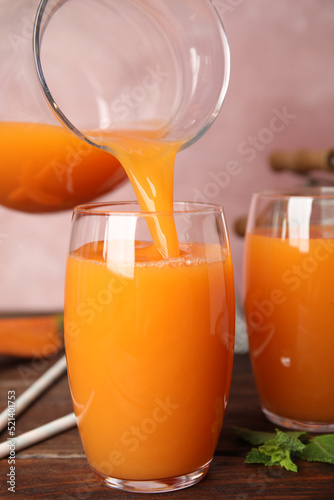 Pouring freshly made carrot juice into glass on wooden table