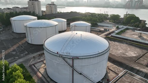 Oil storage tanks in rows along the riverside. Drone aerial view. Oil storage tanks in the sunset time, flying over the tanks along the river.  Industry, business, economy concept b-roll footage.