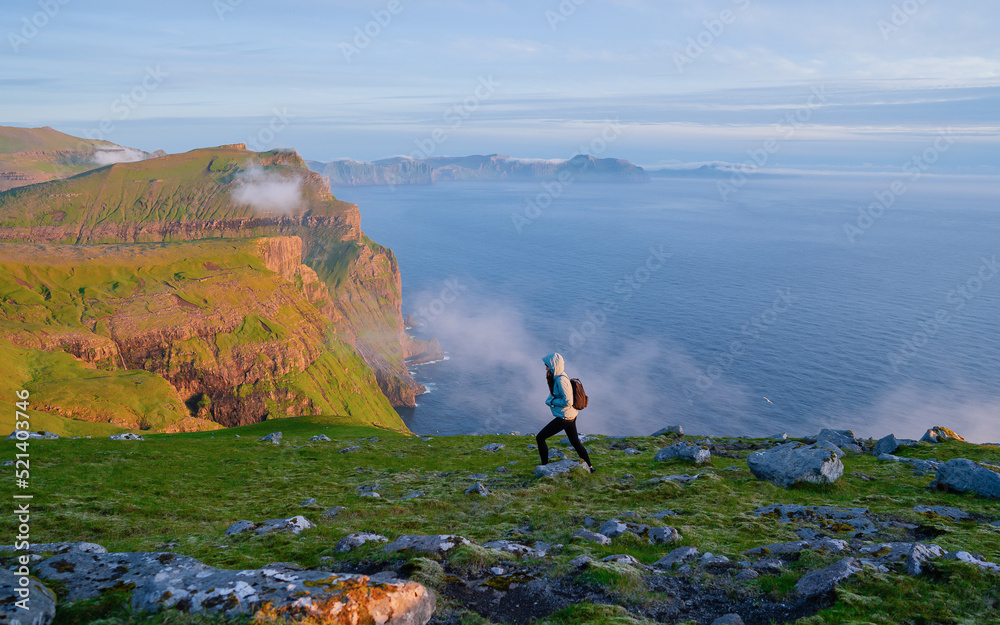An adventurous woman walks on top of a mountain and enjoys a beautiful view during a vivid sunset. Backpacking on top of a mountain cliff landscape and trekking in it. An adventurous woman walks on top of a mountain and enjoys a beautiful view during a vivid sunset. Backpacking on top of a mountain cliff landscape and trekking in it.
