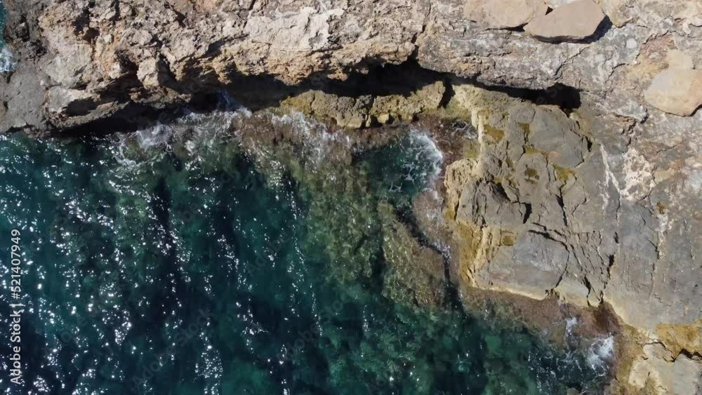 Waves break on stone formations of bay.
Unbelievable aerial view flight bird's eye view drone footage
of cliff edge beach Sa Figuera borda Ibiza summer 2022. 4k Cinematic from above by Philipp Marnitz