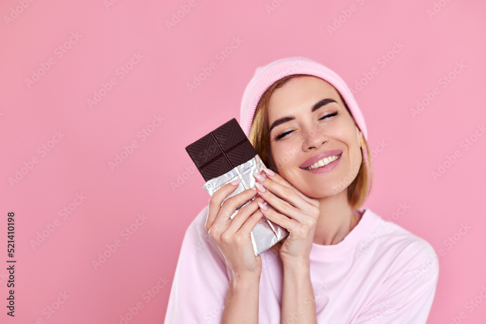 woman enjoying dark chocolate on pastel pink background woman enjoying dark chocolate on pastel pink background