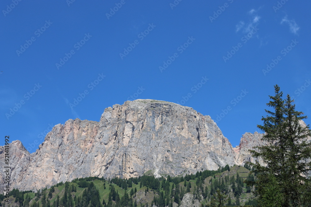Coravara, Italy-July 16, 2022: The italian Dolomites behind the small village of Corvara in summer days with beaitiful blue sky in the background. Green nature in the middle of the rocks. Coravara, Italy-July 16, 2022: The italian Dolomites behind the small village of Corvara in summer days with beaitiful blue sky in the background. Green nature in the middle of the rocks.
