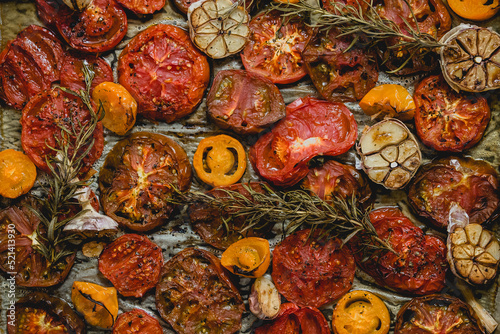 Various kinds of roasted red and yellow tomatoes with thyme and garlic on an metal oven tray
