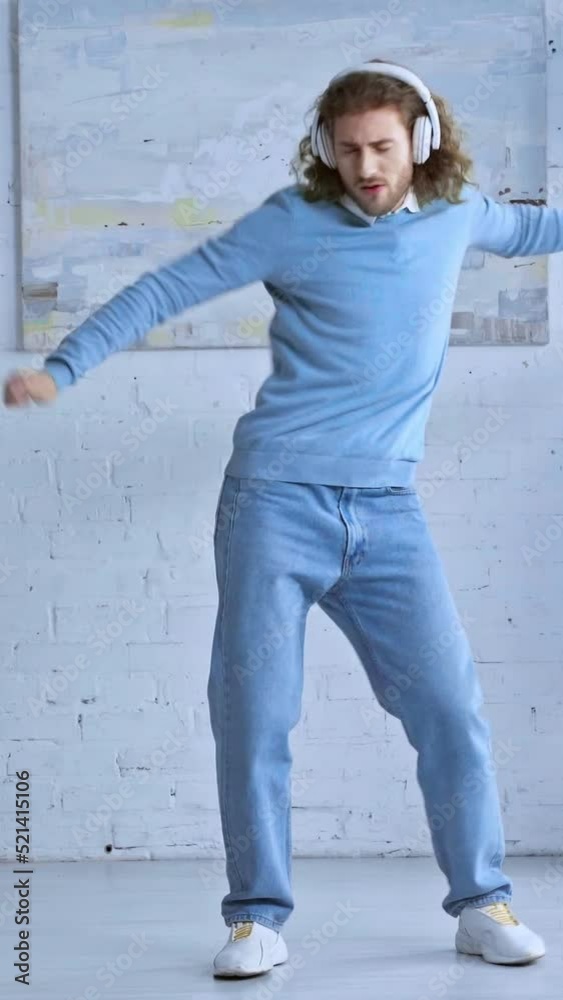 vertical video of happy man in wireless headphones dancing in office