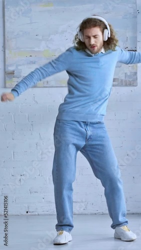 vertical video of happy man in wireless headphones dancing in office