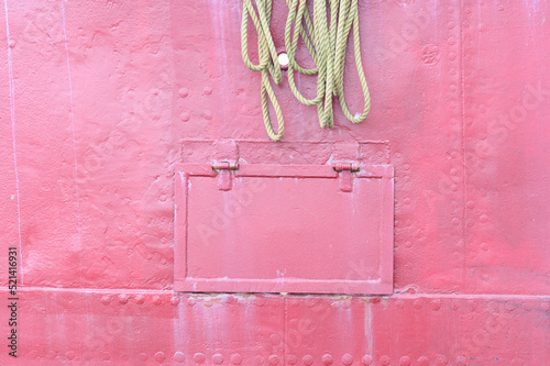 rosafarbener Ausschnitt einer Bordwand eines Schiffes mit einem Tampen photo