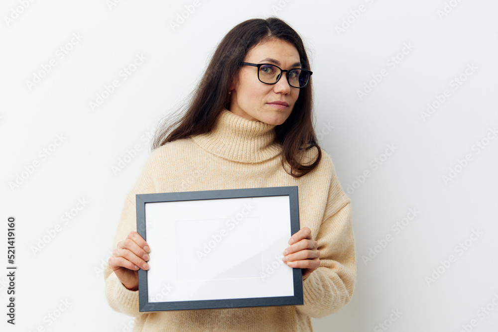 attractive woman with long dark hair, smiling cutely looking at the camera, standing in a sweater with a black frame in her hands on a light background. Studio photography with space for mockup attractive woman with long dark hair, smiling cutely looking at the camera, standing in a sweater with a black frame in her hands on a light background. Studio photography with space for mockup