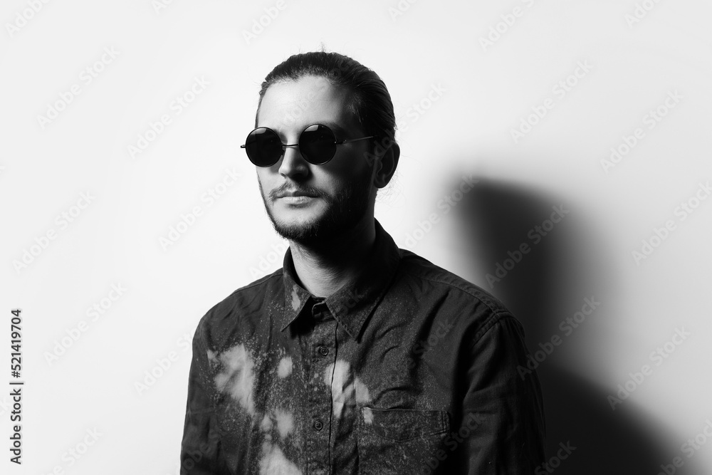 Fototapeta premium Black and white studio portrait of young handsome man with beard, wearing shades.
