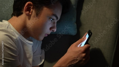 Tired teenager boy text messaging on phone, then yawning. Closeup of handsome guy laying on couch at night