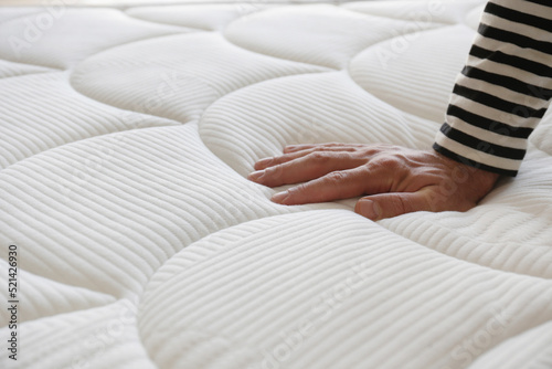 Cropped shot of man testing white orthopedic matress on firmness. Male pressing hypoallergenic foam mattresses surface to check its softness. Close up, copy space, top view, background.