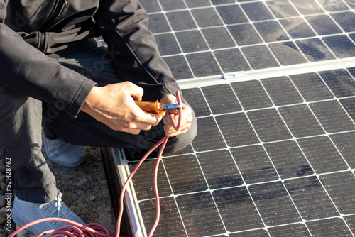 Close up view of unrecognizable man hands cutting a red electricity wire with a plier and solar apnels in the background photo