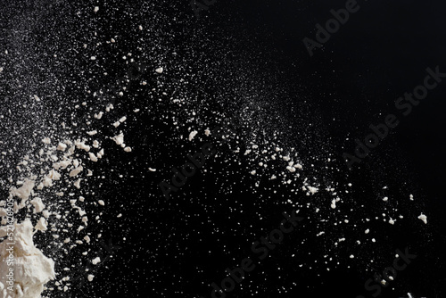 Flying white flour, powder on a black background. Spray of particles, lumps, pieces of white matter.Sweeping dry dust, paint, farina