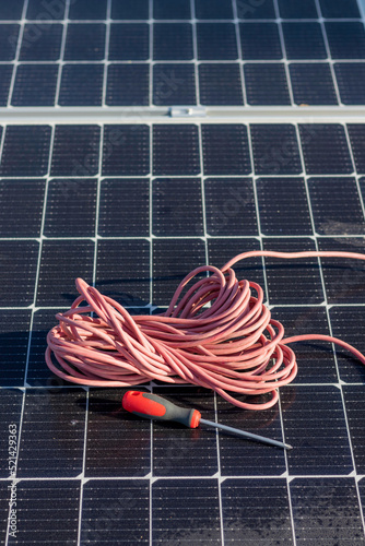 Vertical top view of red cable reel and a screwer leaning on a solar panel installation for renewable energy source