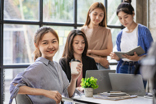 Portrait of Asian woman sitting in front of desk and smiling in office, background view. interactive whiteboard Colleagues working on projects at the financial business concept desk