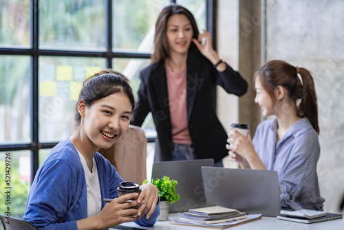 Portrait of Asian woman sitting in front of desk and smiling in office, background view. interactive whiteboard Colleagues working on projects at the financial business concept desk