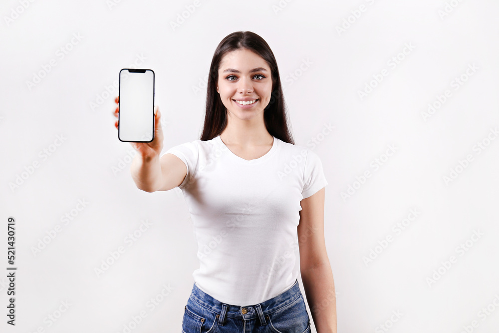 Young beautiful brunette woman with long hair wearing white t-shirt, posing with a phone over isolated background. Portrait of female model showing blank screen cellphone. Close up, copy space Young beautiful brunette woman with long hair wearing white t-shirt, posing with a phone over isolated background. Portrait of female model showing blank screen cellphone. Close up, copy space