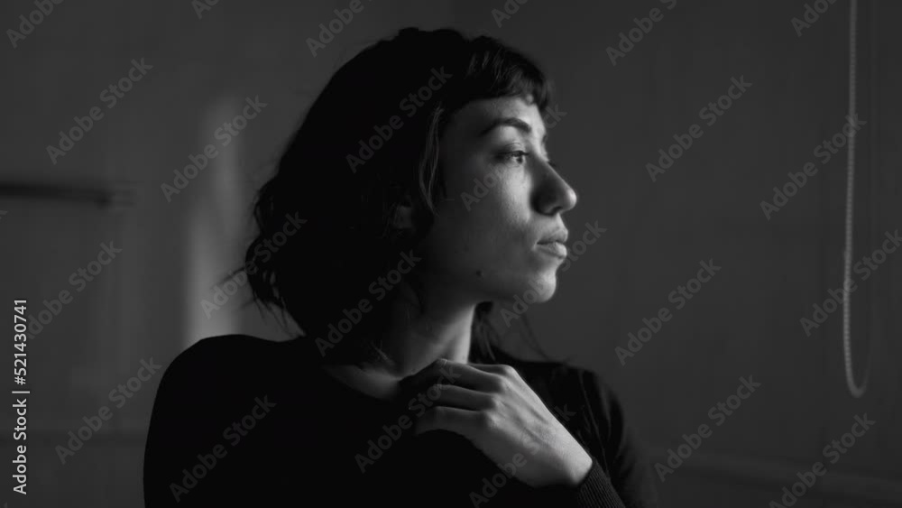 A contemplative young hispanic woman standing by window thinking. A pensive latin girl in monochromatic A contemplative young hispanic woman standing by window thinking. A pensive latin girl in monochromatic